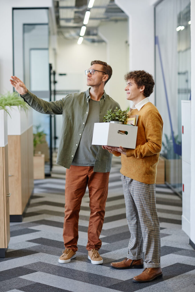 2 Männer im Büro. Einer hält Kiste mit Büromaterialien und beginnt neuen Job